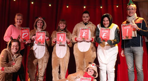 8 Personen. Viele im Rentier-Kostüm, einer als Pinguin verkleidet. Sie halten roter Schilder mit Buchstaben hoch die das Wort DANKE! bilden.