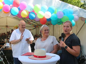 Ein Mann applaudiert. 2 Frauen am Stehtisch. Dahinter volles geschmücktes Festzelt.