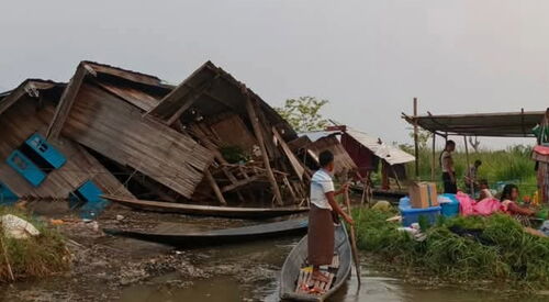 Spendenaufruf für die Opfer des Erdbebens in Myanmar. Foto: zertrümmerte Häuser ein Mann der mit einem improvisierten Kanu zu den Menschen fährt.