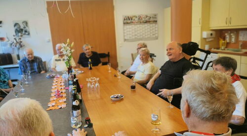 Alte Frauen und Männer an einem großen Tisch. Auf dem Tisch stehen Getränke und Gläser.