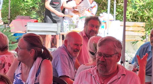 Mehrere Menschen sitzen im Schatten unter Pavillons.