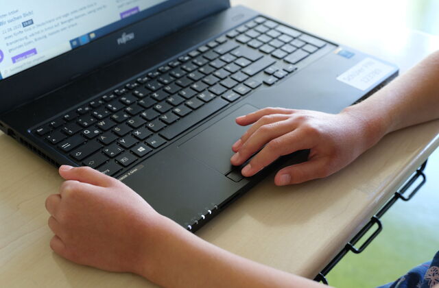 Aufgeklappter Laptop, Schüler Laptop. Kinderhand bedient das Touchpad.