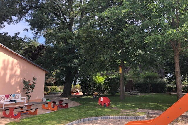 Spielplatz und Bänke zum Ausruhen, Sonne scheint, aber viel Schatten durch Bäume.