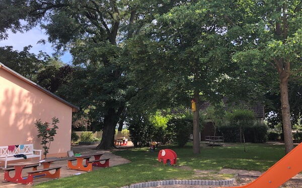 Spielplatz und Bänke zum Ausruhen, Sonne scheint, aber viel Schatten durch Bäume.