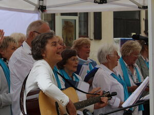 Gemischter Chor. Eine Person mit Gitarre die anderen Klatschen und Singen.