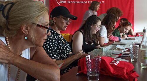 Frauen sitzen an einem Tisch. Auf dem Tisch: Gläser, Wasserflaschen, Stadtpläne.
