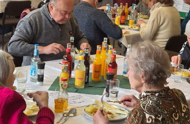 Menschen an Tischen beim Essen, es gibt Spargel und Getränke stehen auf den Tischen. Gemeinsames Mittag.