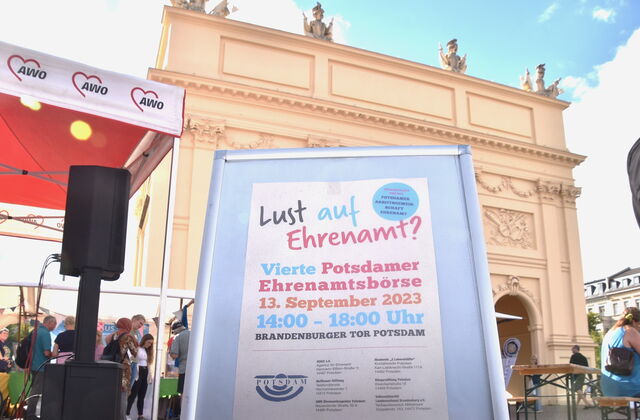 Draußen, schönes, sonniges Wetter. Das Brandenburger Tor in Potsdam im Hintergrund. Ein Aufsteller verkündet die vierte Potsdamer Ehrenamtsbörse am 13.September 2023 14 bis 18 Uhr.