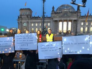 Der Reichstag in Berlin, davor Menschen mit Plakaten. Text auf den Plakaten: Wenn Ihr uns nicht mal verstehen könnt, wie sollen wir euch dann von unseren Diskriminierungen erzählen? - Ohne unsere ADS bleiben wir sprachlich isoliert von der Welt! usw.