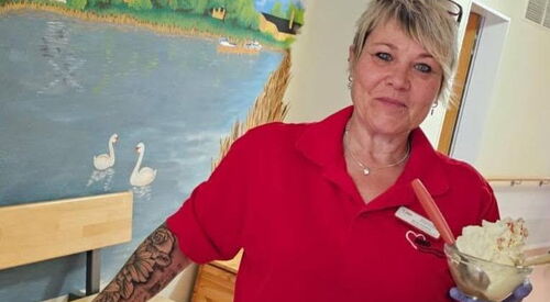 Frau im roten T-Shirt hält Eisbecher mit Sahne in der Hand.