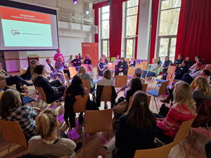 Sehr großer Saal, vier Stuhlkreise, viele Menschen. Oben links eine Leinwand an die das Thema es Fachtags projiziert wird: Unsichtbar? Perspektiven wohnungsloser Frauen.