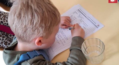 Ein kleiner blonder Junge schreibt mit einem Stift auf einem Formular