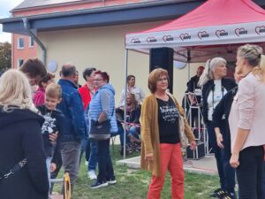 Draußen. Ein roter AWO Pavillon. Menschen stehen in kleinen Gruppen beieinander.