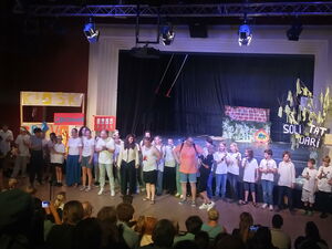 Viele Darsteller vor einer Bühne. Zuschauer im Dunkeln.