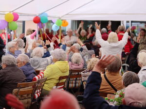 Viele meist ältere Menschen sitzen unter Pavillons. Viele strecken die Arme nach oben.