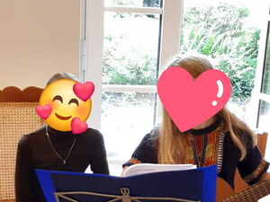 2 Kinder, eine mit Gitarre. Beide sitzen. Gesichter unkenntlich durch Emojis.