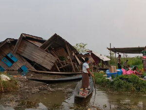 Spendenaufruf für die Opfer des Erdbebens in Myanmar. Foto: zertrümmerte Häuser ein Mann der mit einem improvisierten Kanu zu den Menschen fährt.