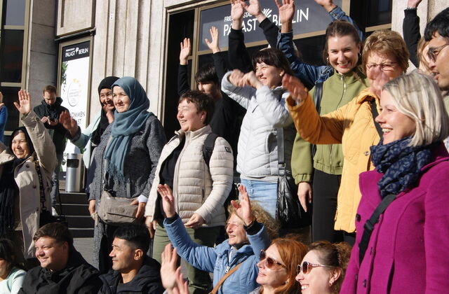 Vor dem Friedrichstadt-Palast Berlin stehen Menschen, einige winken mit beiden Händen über dem Kopf. Fröhliche Gruppe.