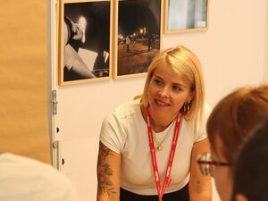 Teamarbeit. Flipchart an der Wand und eins auf eimem Tisch. Blonde Frau mit einem Stift, notiert Ideen der Teilnehmenden.