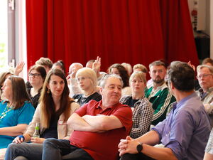 Saal. Teilnehmende. Einige heben die Hand.