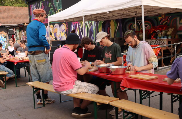 Draußen. Junge Männer an Biertischgarnitur beim Essen zubereiten.