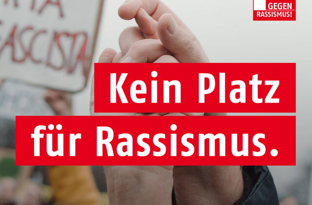 AWO Logo oben in der Ecke. Text: Kein Platz für Rassismus. | Demokratie macht Zukunft. Szene einer Demonstration verschwommen im Hintergrund. Zwei erhobene Hände die sich festhalten.