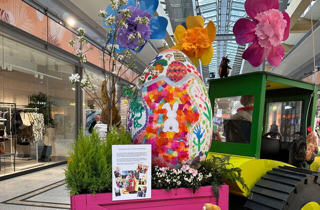 Im Sterncenter. Osterdekoration im Gang. Trecker mit Anhänger. Im Anhänger großes Osterei. Blumen und der Osterhase.