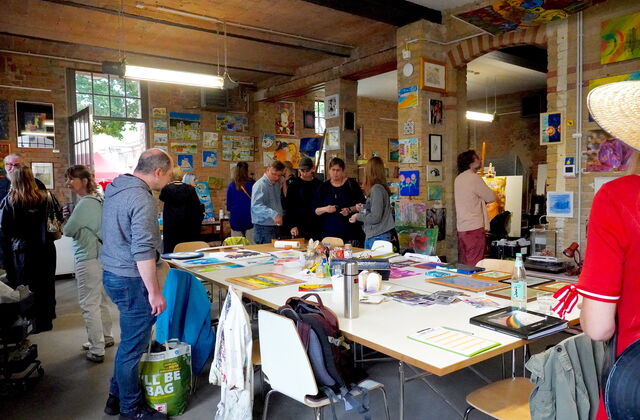 Atelier. Großer Raum mit Bildern an den Wenden. Menschen schauen sich die Kunst an.