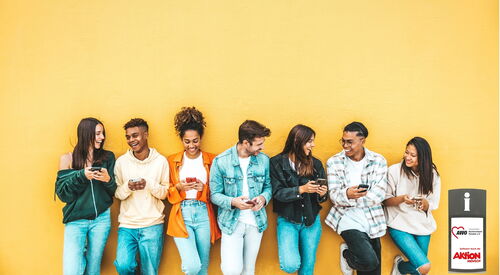 7 junge Menschen lehnen mit dem Rücken lässig an einer gelben Wand. Alle mit Smartphone in der Hand lachen und wirken gelassen.