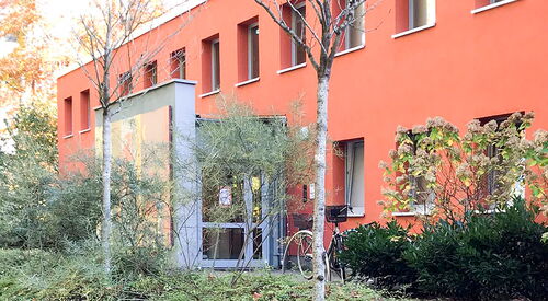 Rotes Gebäude. Vom Gehweg, sind vier Stufen zu einem Weg der zum Eingang des Gebäudes führt.