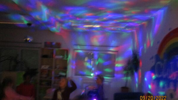 Kinder tanzen in einem abgedunkelten Raum mit bunter Beleuchtung.