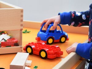 Spieletisch mit Lego und keinem Auto. Eine Kinderhand schiebt das kleine blaue Auto.