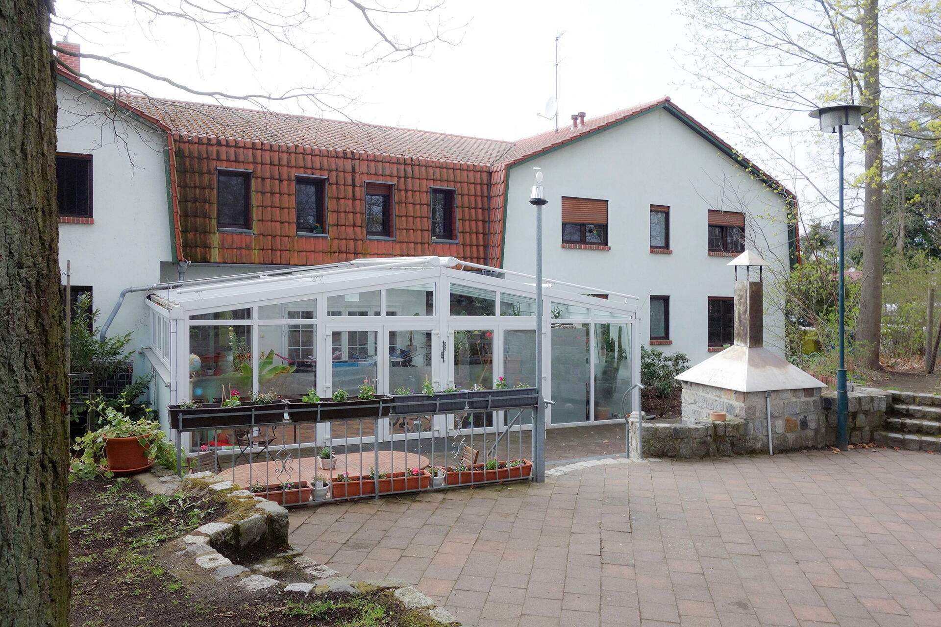 Rückansicht vom Haus mit weißer Fassade und rotem Dach. Ein Wintergarten sowie ein kleiner steinerner Kamin / Ofen für Pizza / Brot mit Schornstein.