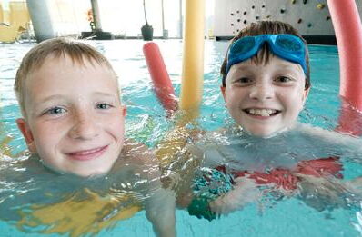 2 fröhliche Kinder beim schwimmen im Hallenbad.