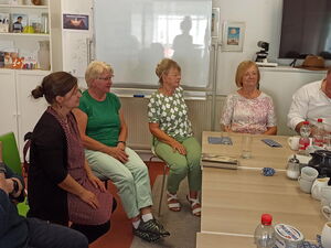 5 Frauen sitzen am Tisch. Ein Mann mit weißem Hemd sitzt rechts hinten am Tisch.