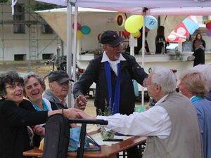Ältere Menschen sitzen an Biertischgarnitur. Halten sich bei den Händen und schunkeln.