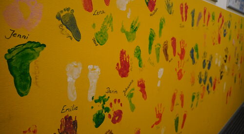 Farbige Fuß- und Handabdrücke auf einer gelben Wand.