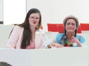 Politikerin und Clownin am Rednerpult. Kinder in Saal.