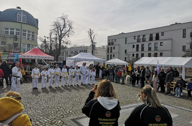 Großer Platz. Außen steh Gäste und in der Mitte eine Reihe Karateschüler in weißer Kleidung mit gelben bzw. weißen Gürtel.