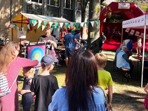 Fest, Das Wurfspiel mit Klettbällen, eine rote Hüpfburg und bunte Stände mit Wimpeln und Luftballons geschmückt. Kinder und Erwachsene in sommerliche Kleidung.