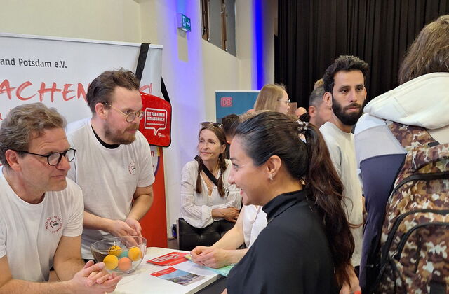 AWO Stand in einer Messehalle. 2 Männer in weißen T-Shirts mit AWWO Logo informieren eine Frau die am Stand steht.