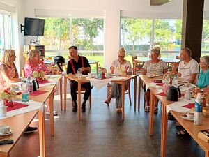 Tische in U Form gestellt. 14 Menschen sitzen an den Tischen. Auf den Tischen Kaffee, Wasser, Tee und Kuchen.