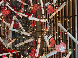 Viele gerollte Wunschzettel hängen an einer Wand mit lichterkette geschmückt.