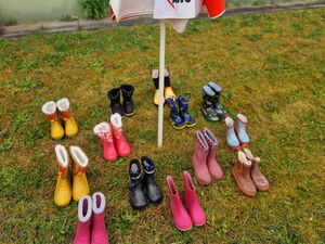 Mehrere Paare Kindergummistiefel stehen unter einem geschlossenen AWO Schirm.