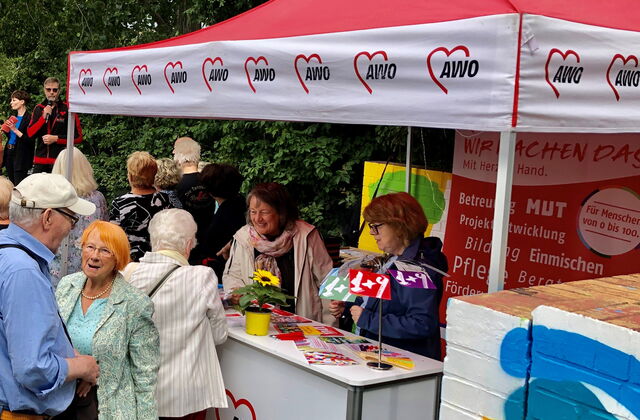 Stand der AWO Potsdam, roter Pavillon. Zwei Frauen stehen am Stand der AWO und beraten. Einige ältere Menschren stehen drum rum und unterhalten sich.