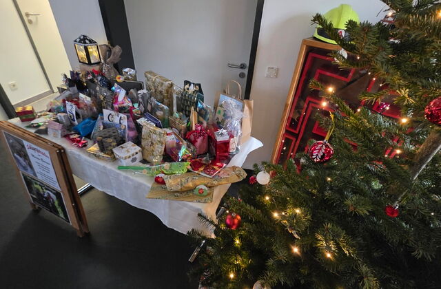 Links: Tisch mit Geschenken und Geschenttüten, rechts: geschmückter Weihnachtsbaum mit roten Kugeln und Lichterkette.