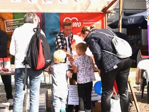 Draußen, Sonne. AWO-Stand. Zwei Kinder und zwei Erwachsene von hinten. Sie stehen am AWO Stand.