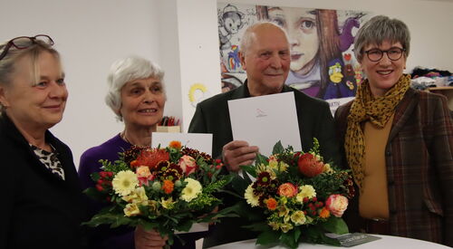 4 Personen stehen um einen Stehtisch. Ältere Frau und älterer Mann sind in der Mitte und halten Freude strahlend ihre Blumen in der Hand. Festlicher Anlass.