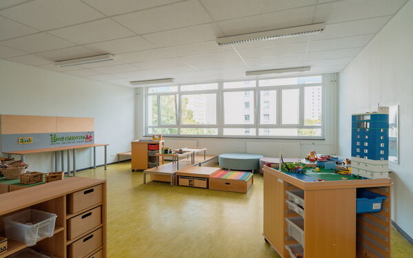 Spielzimmer. Viel Platz, große Fenster. Sitzmöbel bei den Fenstern. Lego Tisch mit Hochhaus bebaut.