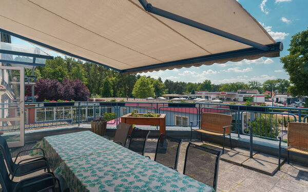 Terrasse mit Markise, darauf ein langer Tisch mit Stühlen.